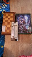 Photo showing the wooden chess board, boxed fantasy puzzle, and packaged thermometer on floor.