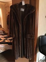 Full view of the dark brown mink fur coat hanging. Shows length, hood, and fur cuffs.