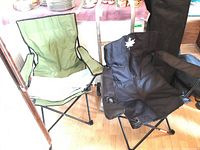 Two folding chairs side by side, one green and one black with maple leaf design.