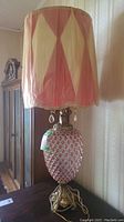 Full view of one lamp showing glass center with red diamond pattern, ornate metal base, and pink and cream diamond-patterned fabric shade with plastic covering