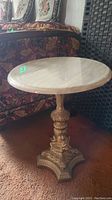 Full view of round marble top table next to a patterned fabric sofa and dark panel.