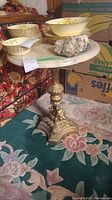 Side view showing marble top with dishes, brass pedestal base, ornate base detailing.
