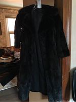 Full-length front view of black mink coat hanging on clear hanger in doorway