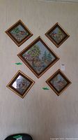 Five framed needlepoint art pieces arranged on a wall, showing the full set and framing style