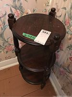 Table shown from an angled top side view, highlighting the round top and two lower shelves with visible scratches.