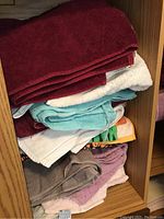 Stack of assorted folded towels in burgundy, white, aqua blue, beige, pink, and brown colors inside wooden shelving
