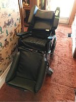Front and side view of the Broda wheelchair with cushioned seating and leg rest.