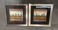 Pair of square-framed landscape paintings with black matting and metallic frames on a grey tiled floor.