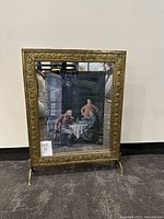 Full view of the brass fireplace stand showing its decorative ornate brass edge and the framed painting in its center.