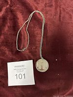 Full view of silver-tone chain necklace with round Stonehenge coin pendant on a red cloth background.