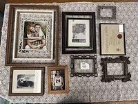 Overview of all 8 picture frames arranged on patterned fabric surface, showing variety of sizes and styles including framed photos and empty frames