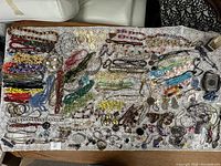 Overview of entire jewelry lot laid out on a lace-like cloth showing the broad variety of pieces including necklaces, pins, brooches, and bracelets.