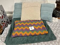 Photo showing the colorful knit blanket folded on top of the large green furry cushion with the assortment of pillows arranged at the back.