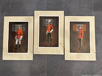 Three framed prints of Canadian Mounties displayed against dark floor, showing full body portraits and beige mats with some wear