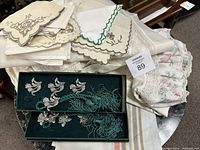 Stack of vintage linens including napkins and bed set pieces in various embroidered and scalloped styles.