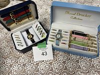 Full set of watches and accessories displayed in two branded boxes on lace tablecloth.