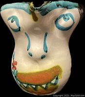 Front view of colorful face pitcher with painted eyes, nose, and mouth with teeth, featuring ceramic chipped spout area.