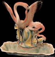 Front view of vintage ceramic flamingo TV lamp with extended wings and smaller flamingos at base in pastel colors.