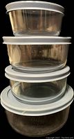 Stacked 4 clear glass containers of different sizes with white lids