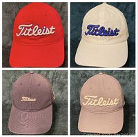 Four golf hats in red, white, blue, and gray with different Titleist logo embroidery styles on front.