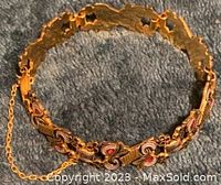 Close-up image of the gold and silver bracelet showing red accents and security chain on a dark fabric background.