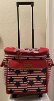Front view of the Arctic Zone rolling cooler showing the red, white, and blue star and stripe fabric design and extended telescopic handle
