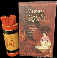 Photo showing Chinese Fortune Sticks guidance book and wooden chim bucket filled with red fortune sticks.