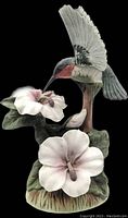 Front and side view of hummingbird figurine perched hovering over two hibiscus flowers, showing paint detail and bisque porcelain texture
