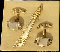 Photo showing the vintage tie bar and pair of cuff links on a yellow satin display card, highlighting the filigree gold and silver design and mother of pearl details.