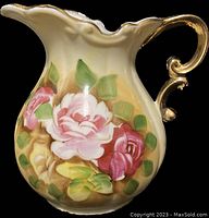 Front side showing floral design with pink, white, and red roses and gold accents on the rim and handle.