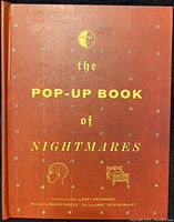Front cover of the book showing title 'the Pop-Up Book of Nightmares' in gold on reddish cover with decorative elements.