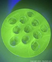Top view of round uranium glass flower frog with 11 holes glowing green under black light.