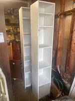 Two tall white bookcases standing side by side in a workshop or garage environment. Shelves are visible, and surfaces show signs of wear.