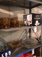 Glass shelf showing 4 amber stemmed glasses, 7-piece Simply White soup set box, large clear glass bowl, and medium wavy glass bowl.