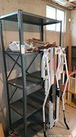 Full view of the empty metal shelving unit in a basement environment showing all five shelves and surrounding stored items.