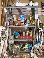 Front view of gray metal shelving unit showing four shelves with various items placed on them; rust spots and wear visible on shelves and frame.