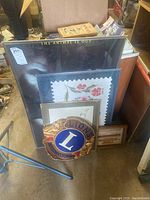 Shows Lions Club plaque in front of framed prints and posters stacked on floor.