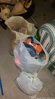 Three bags on floor; largest bag contains assorted yarn including orange, green, and blue skeins; medium bag includes sewing patterns, one Halloween themed; smallest bag appears to contain scrap fabric.