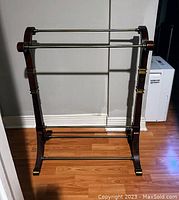 Full view of the wooden and brass blanket/quilt hanger showing the frame, brass bars, and floor placement.