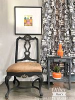 Front view of black painted wooden chair with open decorative backrest and tan faux leather painted fabric seat with a stamped design.