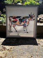 Photo of framed cow print showing multicolored abstract cow and frame in outdoor setting with natural light.