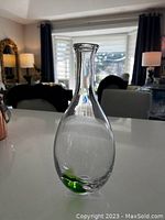 Photo showing the clear glass bottle with a bulbous shape and narrow neck, light green base visible.