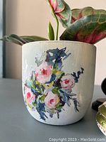 Close-up of the hand painted flower pot showing detailed floral motif of pink and white flowers with green and blue leaves on a white base.