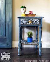 Full view of blue hand painted night table with decor on top, showing single drawer and lower shelf with floral decoupage pattern.