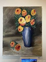 Original chalk paint floral painting on canvas, showing a blue vase with yellow and orange flowers and some loose flowers on table surface.