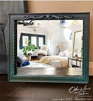 Full view of rectangular mirror showing dark green frame with carved ornate embellishments reflecting a bedroom.
