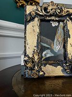 Close-up of corner showing gold leaf and black distressed finish, part of an intricate floral pattern.