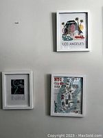 Photo of three white framed vacation prints on a grey wall. The frames contain prints of Los Angeles, NYC, and Rome.