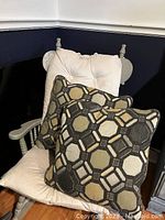 Two brown, grey and beige geometric patterned sofa cushions placed on a beige cushioned chair.