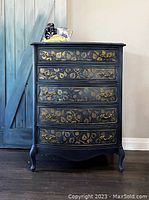 Front view of blue wooden tallboy dresser with four drawers and gold stenciled designs and gold handles